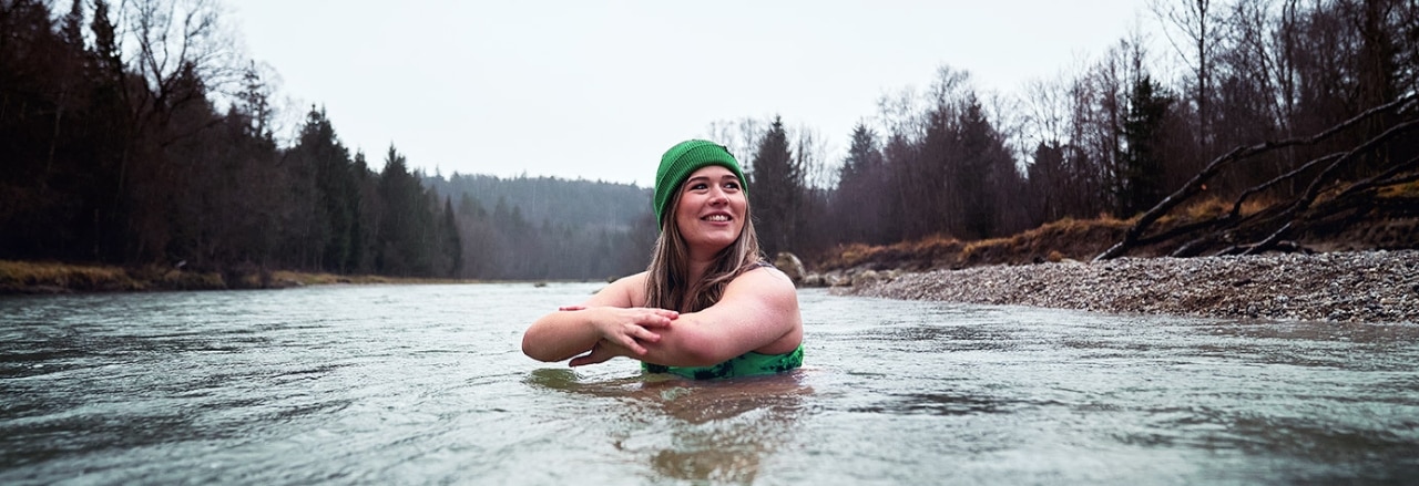 Frau mit grüner Mütze beim Eisbaden in einem Fluss