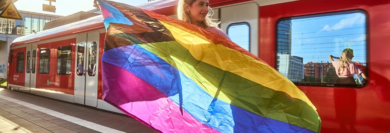 Frau mit Regenbogenflagge steht neben S-Bahn