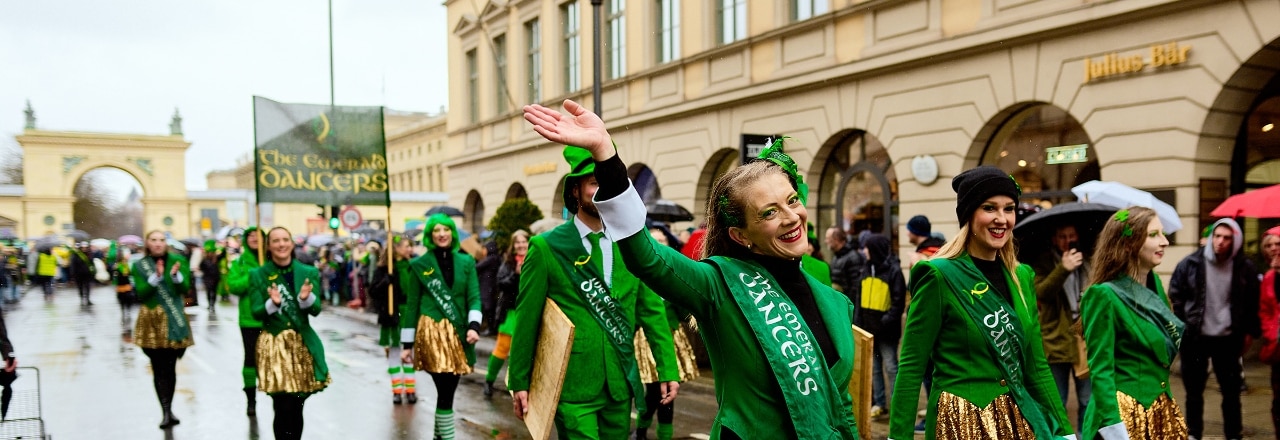 Eine grün gekleidetet Gruppe läuft auf einer Strasse, eine Frau winkt in die Kamera