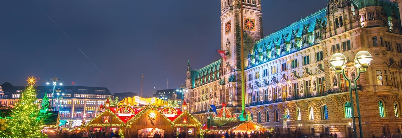 Beleuchtetes Hamburger Rathaus und Weihnachtsmarkt bei Nacht.