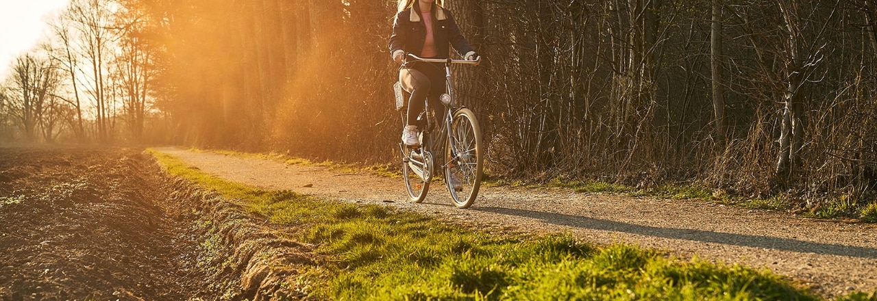 Frau fährt im Sonnenuntergang Fahrrad auf einem Radweg