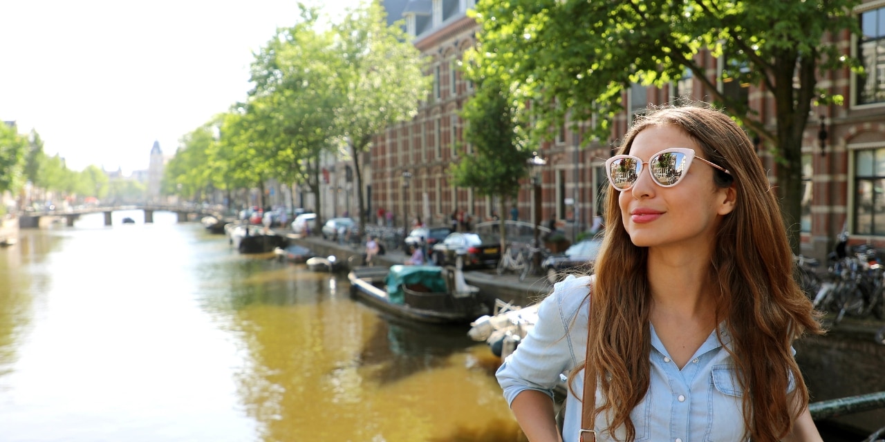 Junge Frau mit Sonnenbrille an einer Gracht in Amsterdam