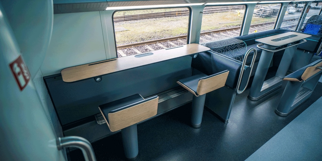 Eine Arbeitstheke am Fenster mit Tablethalterung, zwei Stehhockern und beleuchteten Steckdosen ermöglicht das schnelle Arbeiten von unterwegs.