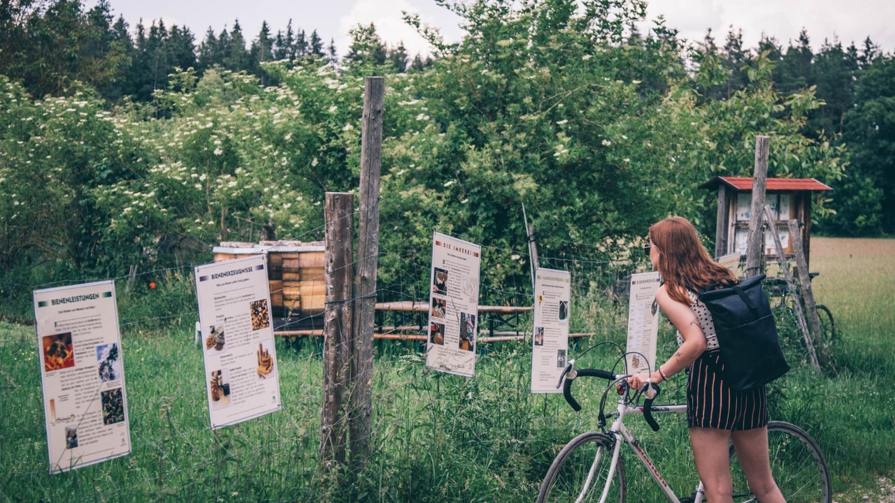 Frau mit Fahrrad liest Schild am Wegesrand