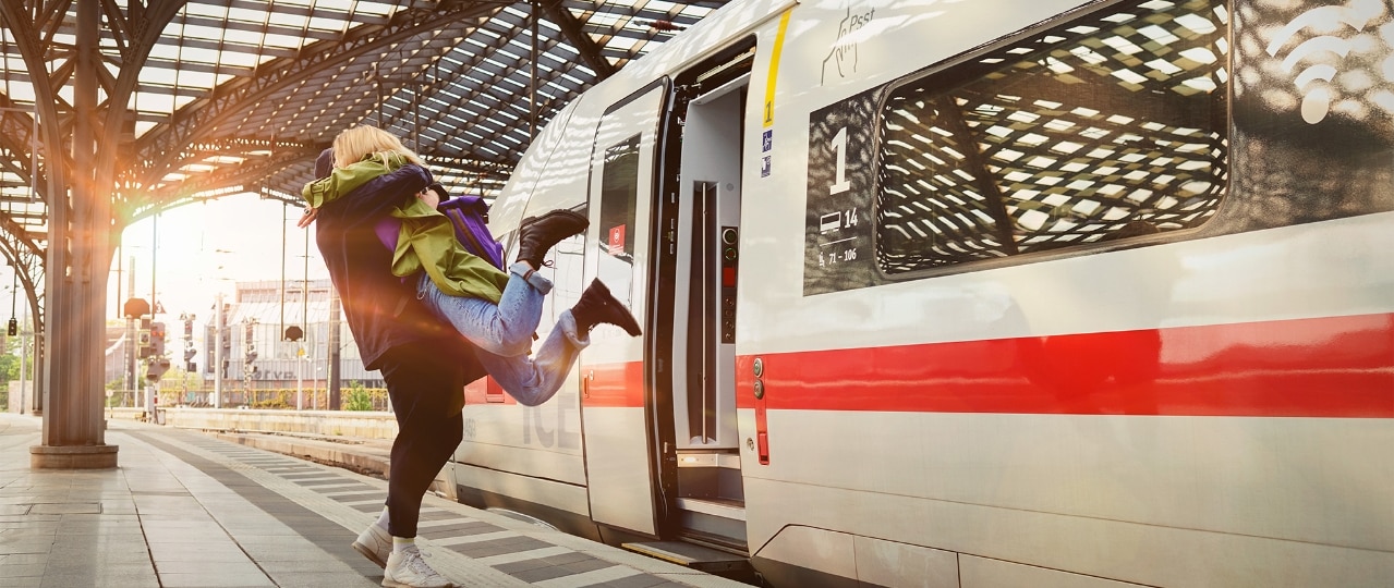 Junges Paar umarmt sich stürmisch am Bahnhof vor einem ICE 