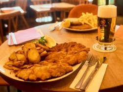 Zwei Teller gefüllt mit Schnitzeln und Kartoffelecken auf Holztisch daneben ein Glas Bier