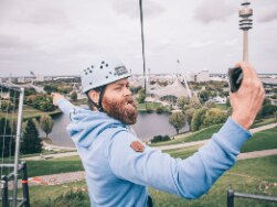 Person mit Kletterhelm im Olympiapark - im Hintergrund der Olympiaturm