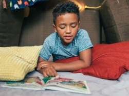 Junge liegt auf einer Decke und liest ein Buch
