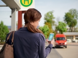 Frau mit Smartphone an der Bushaltestelle