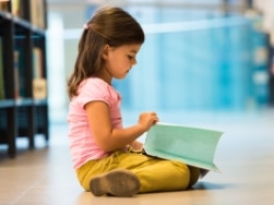 Kleines Mädchen sitzt auf dem Boden und liest ein Buch