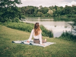 Frau sitzt auf einer Decke am See