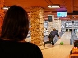 Blick über Schulter von Frau auf Mann vor Bowlingbahn