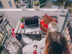 Eine Person sitzt mit einem Laptop auf dem Balkon