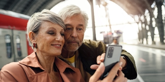 Älteres Paar am Bahnsteig mit Smartphone