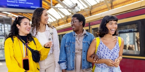 4 junge Reisende stehen vor einem Zug am Bahnhof