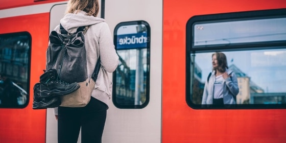 Frau mit Wanderschuhen am Rucksack steht vor der S-Bahn