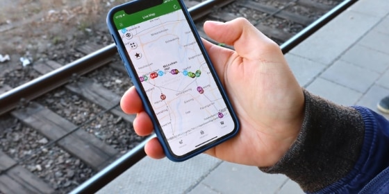 Person hält ein Handy mit der München Navigator App in der Hand