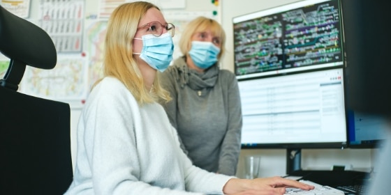 Zwei Frauen mit medizinischer Maske schauen in Computer Bildschirm