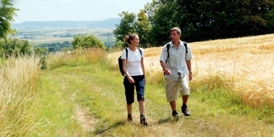 Mann und Frau wandern auf einer Wiese am Feld