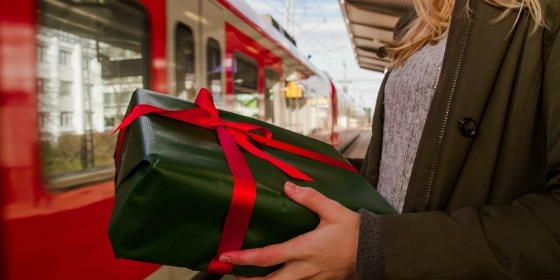 Frau mit einem Geschenk steht am Bahnsteig