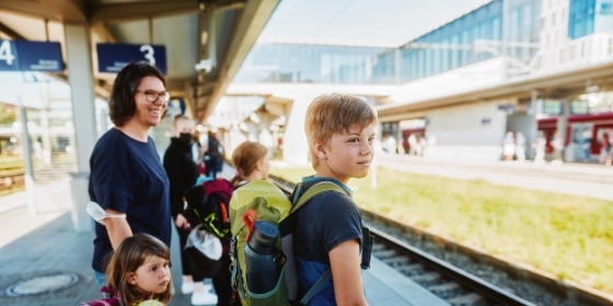 Mutter und Schulkinder stehen am Bahnsteig