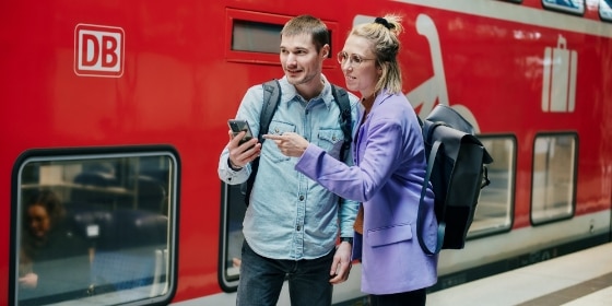 Zwei Menschen am Gleis vor Regionalzug schauen auf ein Handy