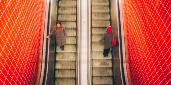 Zwei Personen fahren mit der Rolltreppe