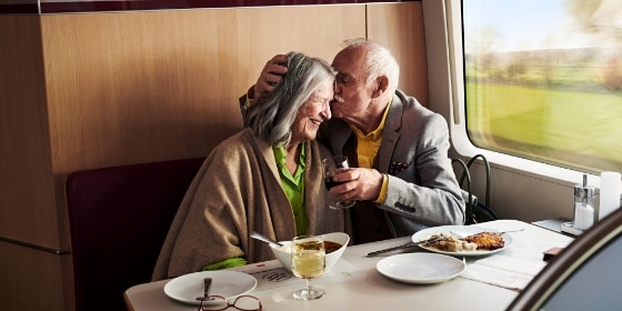 Seniorenpaar lacht im Bordrestaurant; Mann gibt Frau Kuss auf Stirn, die lacht