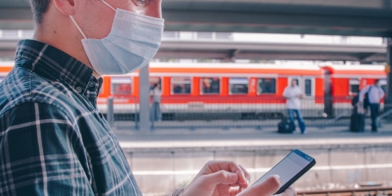 Person mit Mundschutz und Handy am Bahnsteig