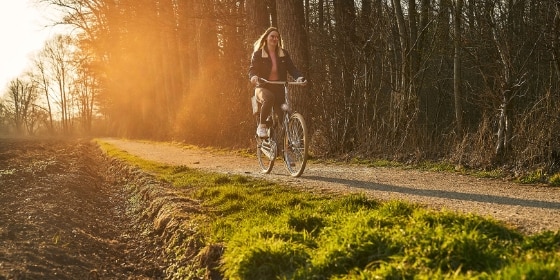 Frau fährt im Sonnenuntergang Fahrrad auf einem Radweg