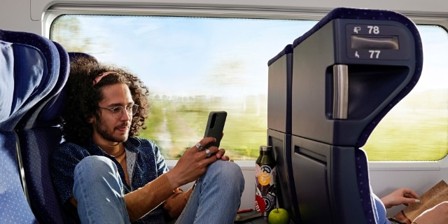 Ein junger Mann sitzt mit angewinkelten Knien auf dem Sitz und schaut auf sein Handy