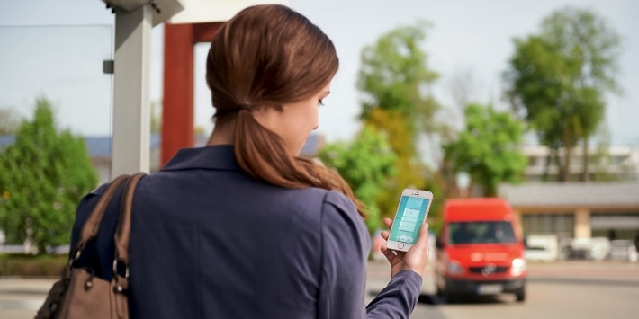 Frau mit Smartphone an der Bushaltestelle