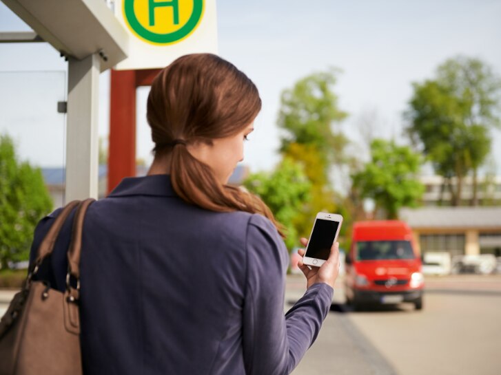 Frau mit Handy an Bushaltestelle