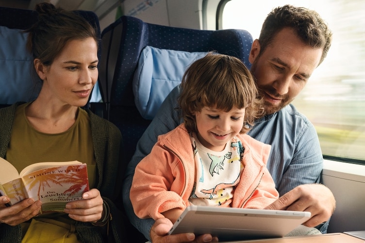 Familie im Zug, schaut auf Tablet.