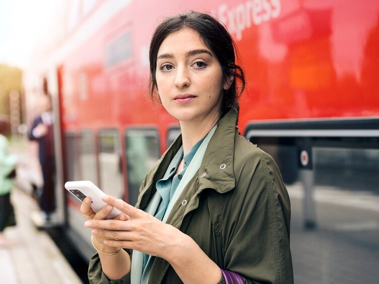 Pendler mit Tasche und Smartphone vor einem Regionalzug