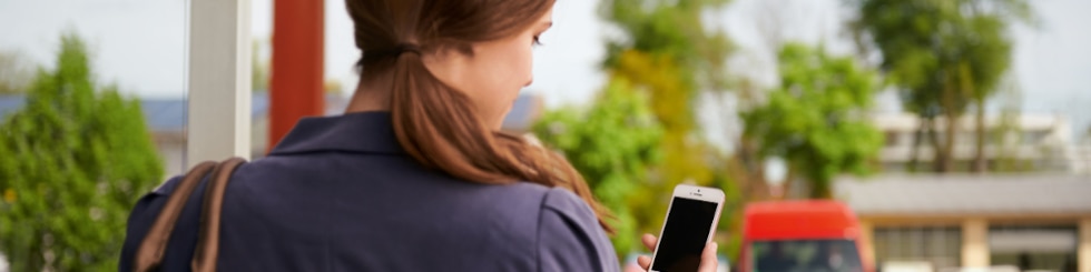 Frau mit Handy an Bushaltestelle