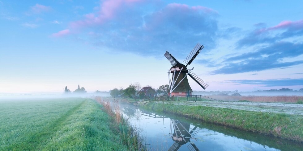 Dutch windmill by river at sunrise