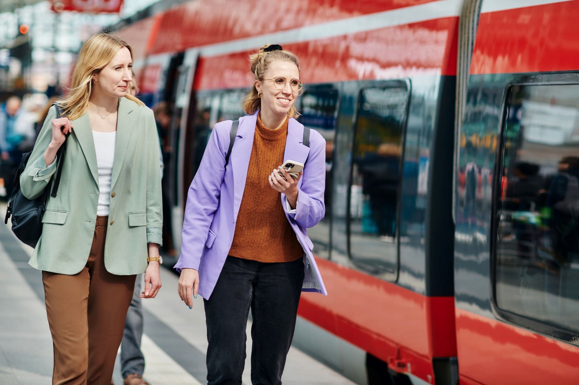 Zwei junge Frauen laufen lachend neben einem Regionalzug am Gleis